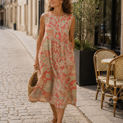 Beth - Robe Midi Florale gedragen in een Parijse lifestyle setting, een mouwloze midi jurk in koraalroze linnen met saliegroene florale print, ronde hals, ontspannen A-lijn pasvorm en zijzakken.