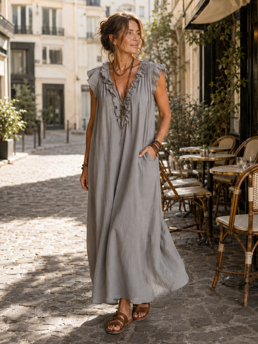 Camélia - Robe Longue Bohème gedragen in een Parijse lifestyle setting, een lange bohemian jurk in steengrijze taupe gewassen stof met diepe V-hals, rucheafwerking, zachte kapmouwtjes en zijzakken.