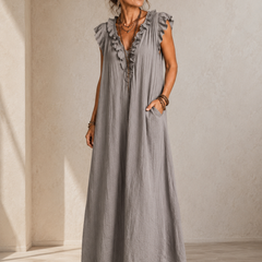 Camélia - Robe Longue Bohème in een luxe studiosetting met warme kalkstenen achtergrond, uitgevoerd in steengrijze taupe stof met gekreukte textuur, diepe V-hals met ruches en een vloeiende maxi pasvorm.