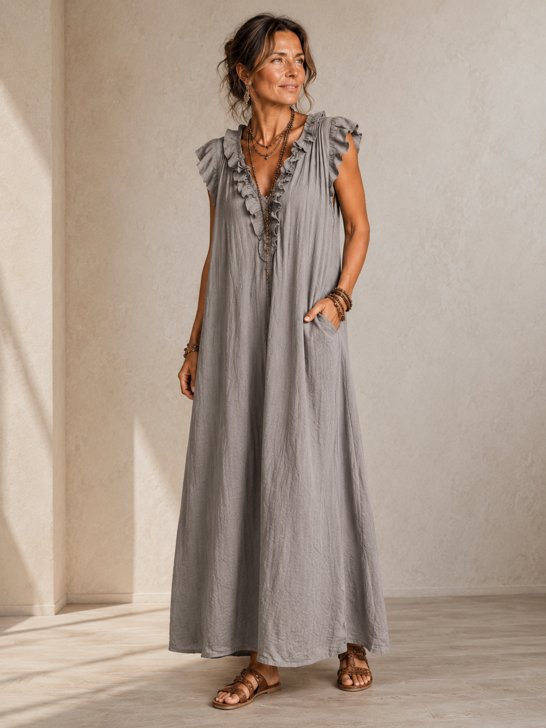 Camélia - Robe Longue Bohème in een luxe studiosetting met warme kalkstenen achtergrond, uitgevoerd in steengrijze taupe stof met gekreukte textuur, diepe V-hals met ruches en een vloeiende maxi pasvorm.