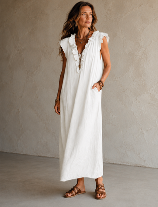 Camélia - Robe Longue Bohème in een luxe studiosetting met warme kalkstenen achtergrond, uitgevoerd in steengrijze taupe stof met gekreukte textuur, diepe V-hals met ruches en een vloeiende maxi pasvorm.