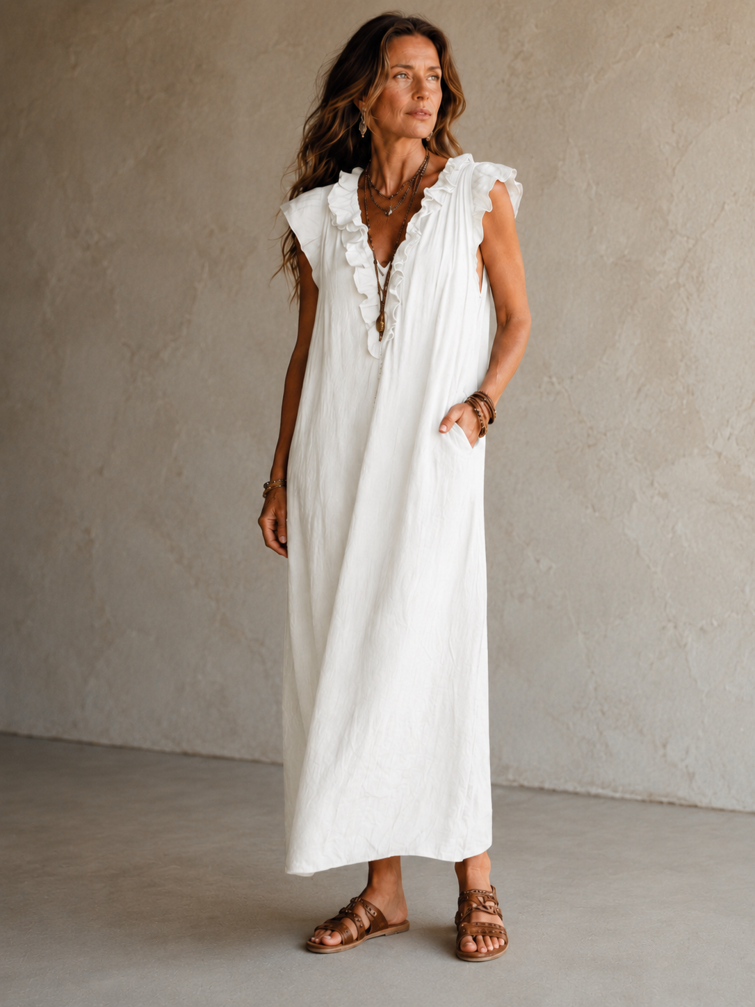 Camélia - Robe Longue Bohème in een luxe studiosetting met warme kalkstenen achtergrond, uitgevoerd in steengrijze taupe stof met gekreukte textuur, diepe V-hals met ruches en een vloeiende maxi pasvorm.