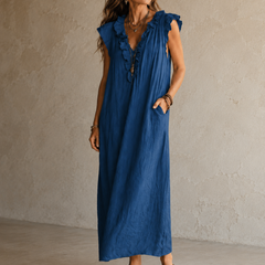 Camélia - Robe Longue Bohème in een luxe studiosetting met warme kalkstenen achtergrond, uitgevoerd in steengrijze taupe stof met gekreukte textuur, diepe V-hals met ruches en een vloeiende maxi pasvorm.