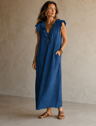Camélia - Robe Longue Bohème in een luxe studiosetting met warme kalkstenen achtergrond, uitgevoerd in steengrijze taupe stof met gekreukte textuur, diepe V-hals met ruches en een vloeiende maxi pasvorm.