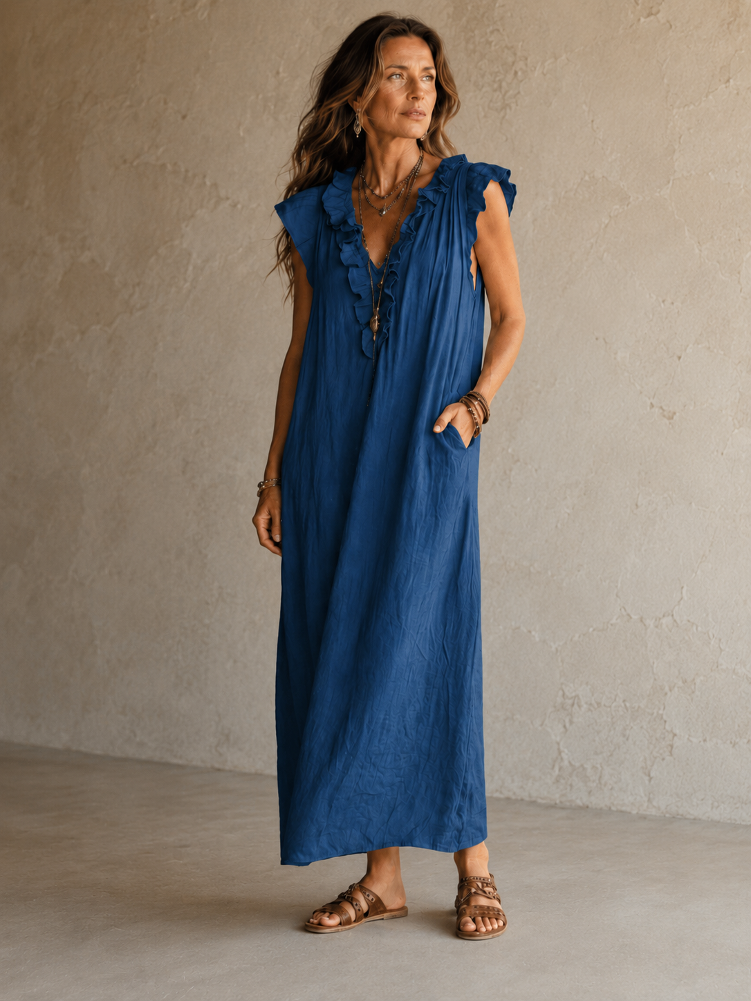 Camélia - Robe Longue Bohème in een luxe studiosetting met warme kalkstenen achtergrond, uitgevoerd in steengrijze taupe stof met gekreukte textuur, diepe V-hals met ruches en een vloeiende maxi pasvorm.