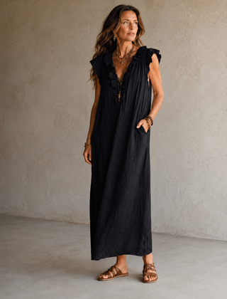 Camélia - Robe Longue Bohème in een luxe studiosetting met warme kalkstenen achtergrond, uitgevoerd in steengrijze taupe stof met gekreukte textuur, diepe V-hals met ruches en een vloeiende maxi pasvorm.