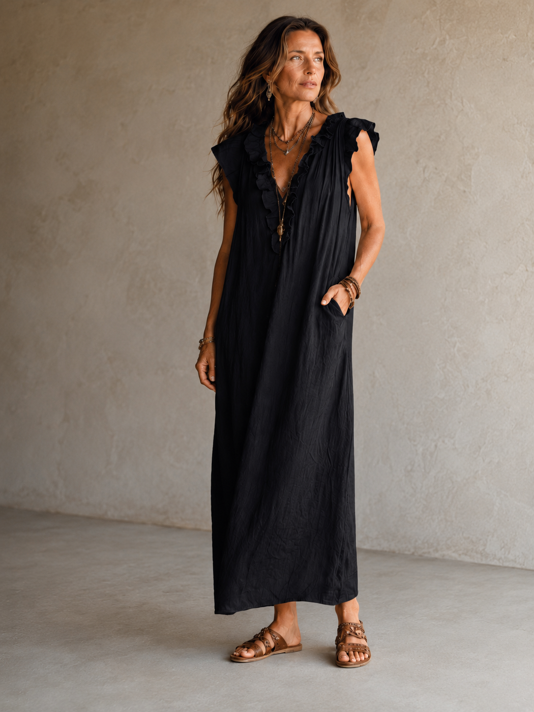 Camélia - Robe Longue Bohème in een luxe studiosetting met warme kalkstenen achtergrond, uitgevoerd in steengrijze taupe stof met gekreukte textuur, diepe V-hals met ruches en een vloeiende maxi pasvorm.