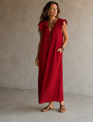 Camélia - Robe Longue Bohème in een luxe studiosetting met warme kalkstenen achtergrond, uitgevoerd in steengrijze taupe stof met gekreukte textuur, diepe V-hals met ruches en een vloeiende maxi pasvorm.