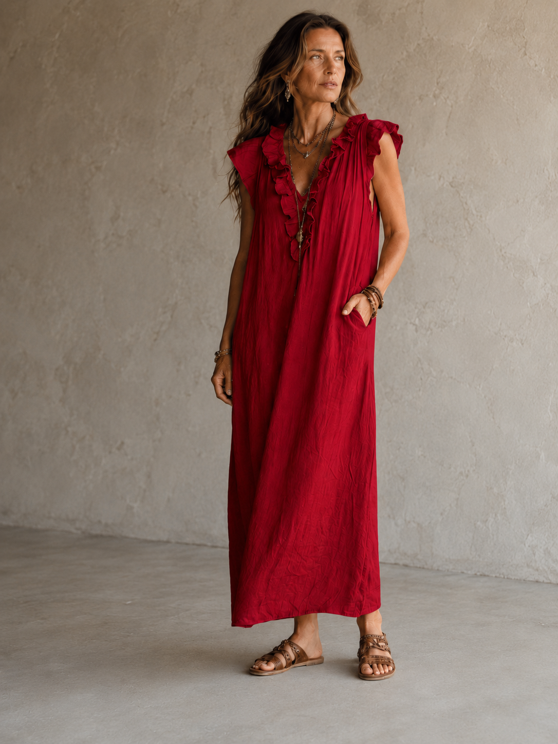 Camélia - Robe Longue Bohème in een luxe studiosetting met warme kalkstenen achtergrond, uitgevoerd in steengrijze taupe stof met gekreukte textuur, diepe V-hals met ruches en een vloeiende maxi pasvorm.