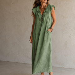 Camélia - Robe Longue Bohème in een luxe studiosetting met warme kalkstenen achtergrond, uitgevoerd in steengrijze taupe stof met gekreukte textuur, diepe V-hals met ruches en een vloeiende maxi pasvorm.