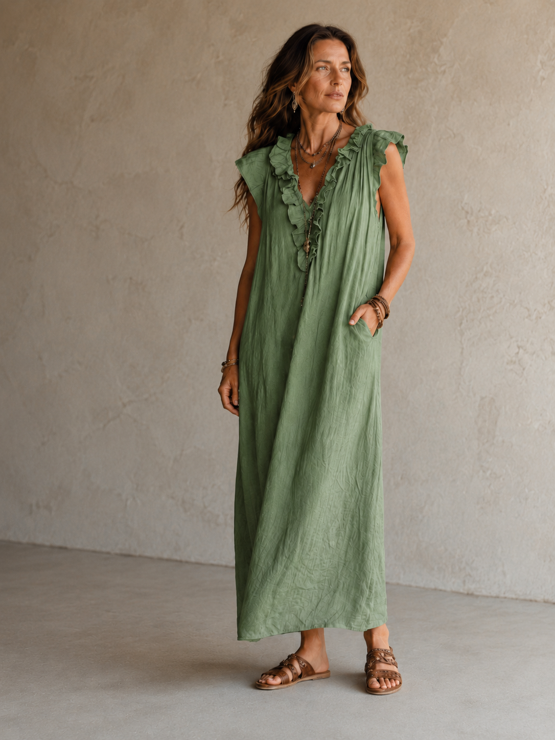 Camélia - Robe Longue Bohème in een luxe studiosetting met warme kalkstenen achtergrond, uitgevoerd in steengrijze taupe stof met gekreukte textuur, diepe V-hals met ruches en een vloeiende maxi pasvorm.